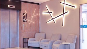 Un vestíbulo moderno con pantalla digital de ascensor, una recepción y un área de estar con sillones y una pequeña mesa.