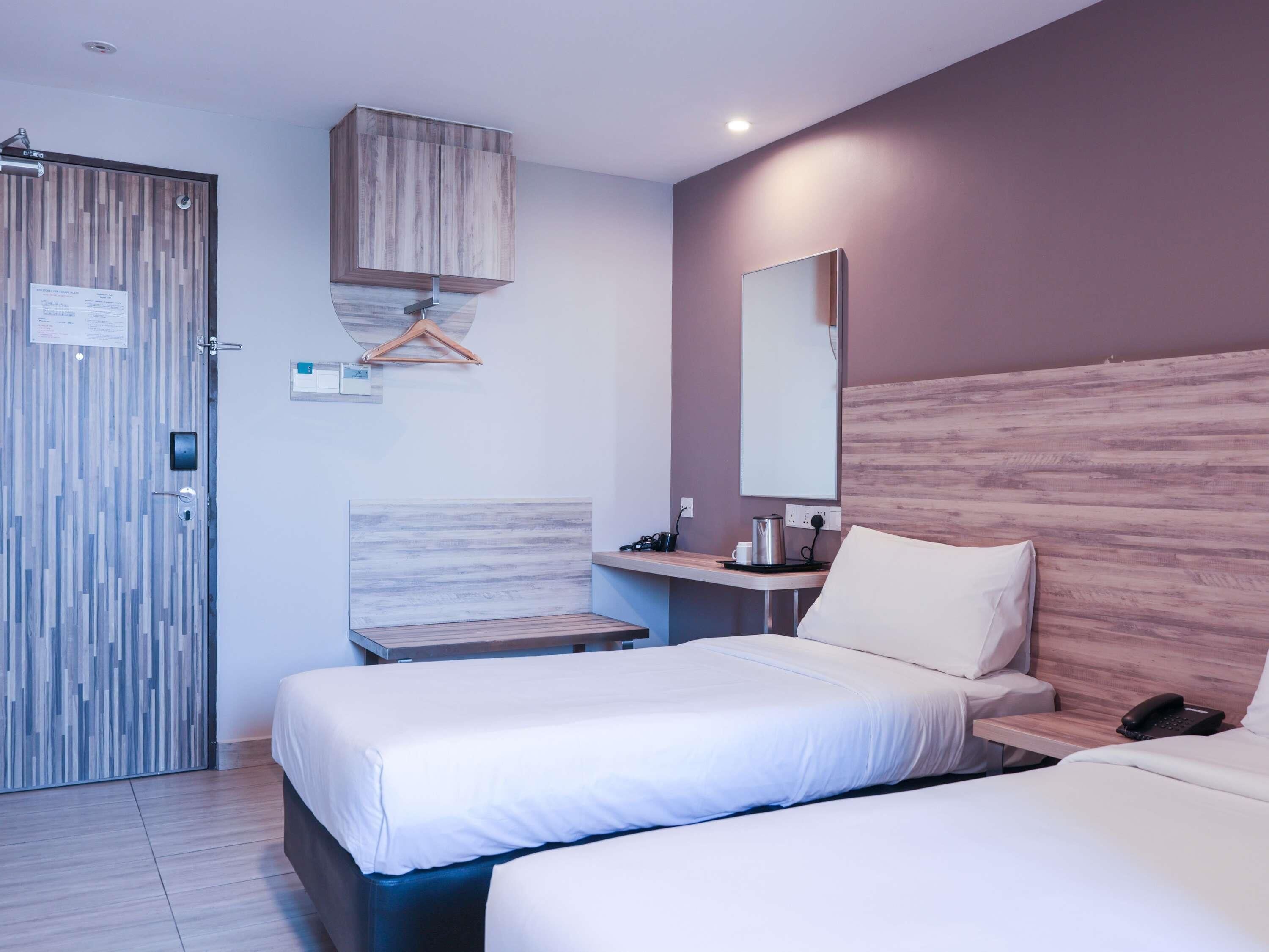 A hotel room with two beds, a desk, a chair, a wardrobe, a mirror, and a bedside table with a phone.