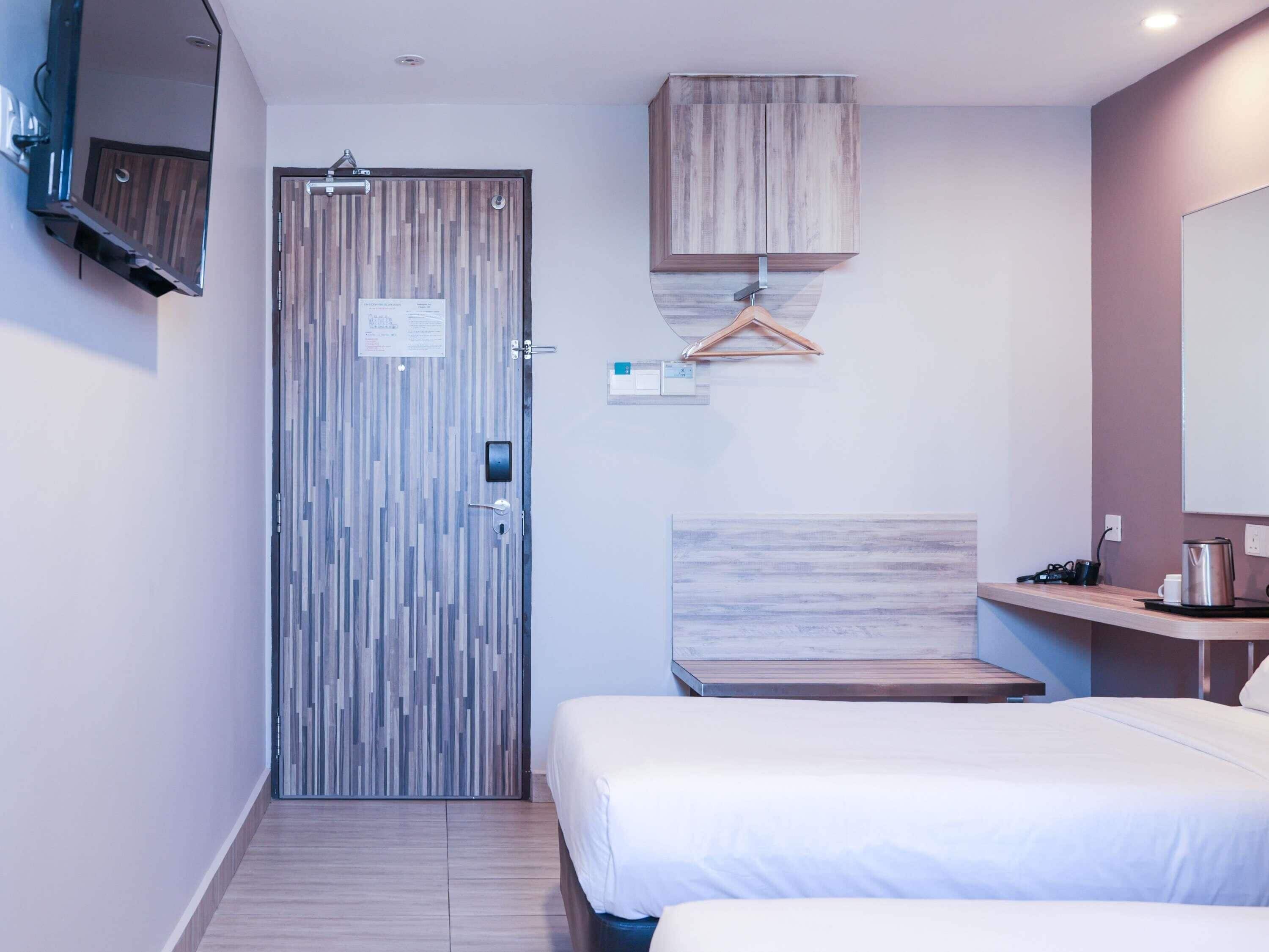A hotel room with a bed, a desk, a mirror, a wardrobe, and a door with a security lock.