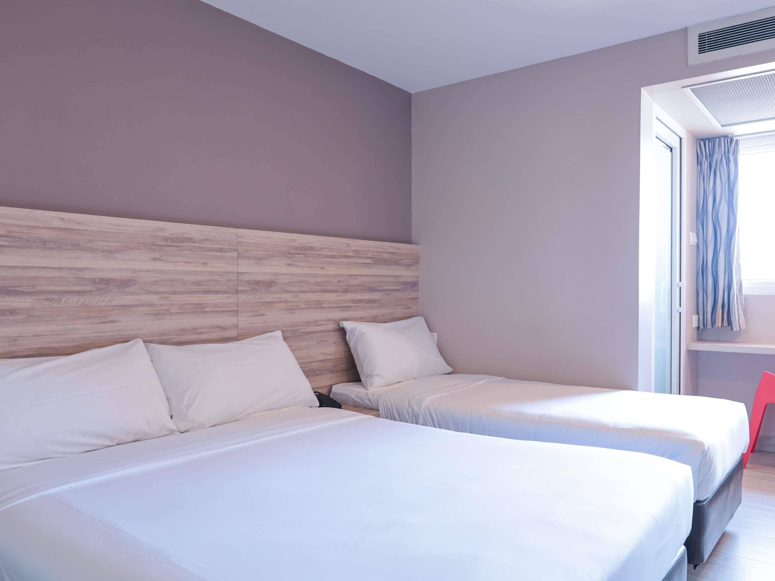 A hotel room with two beds, a wooden headboard, a window with curtains, and a red chair.