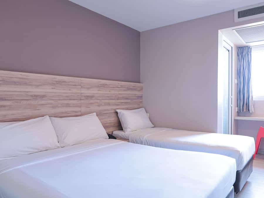 Habitación de hotel con dos camas, cabecero de madera, ventana con cortinas y una silla roja.
