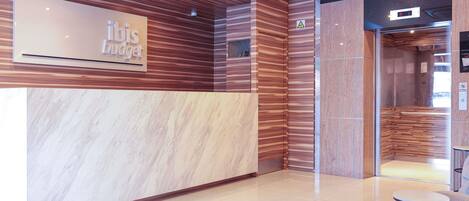 Un área de recepción con mostrador de mármol, paneles de madera y un letrero que dice 'ibis budget'.