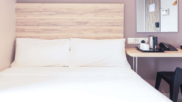 Habitación de hotel con cama, escritorio con teléfono, cafetera y una silla.