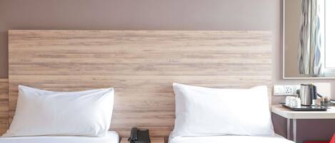 A hotel room with two beds, a wooden headboard, a bedside table with a telephone, a red chair, and a wall-mounted artwork.