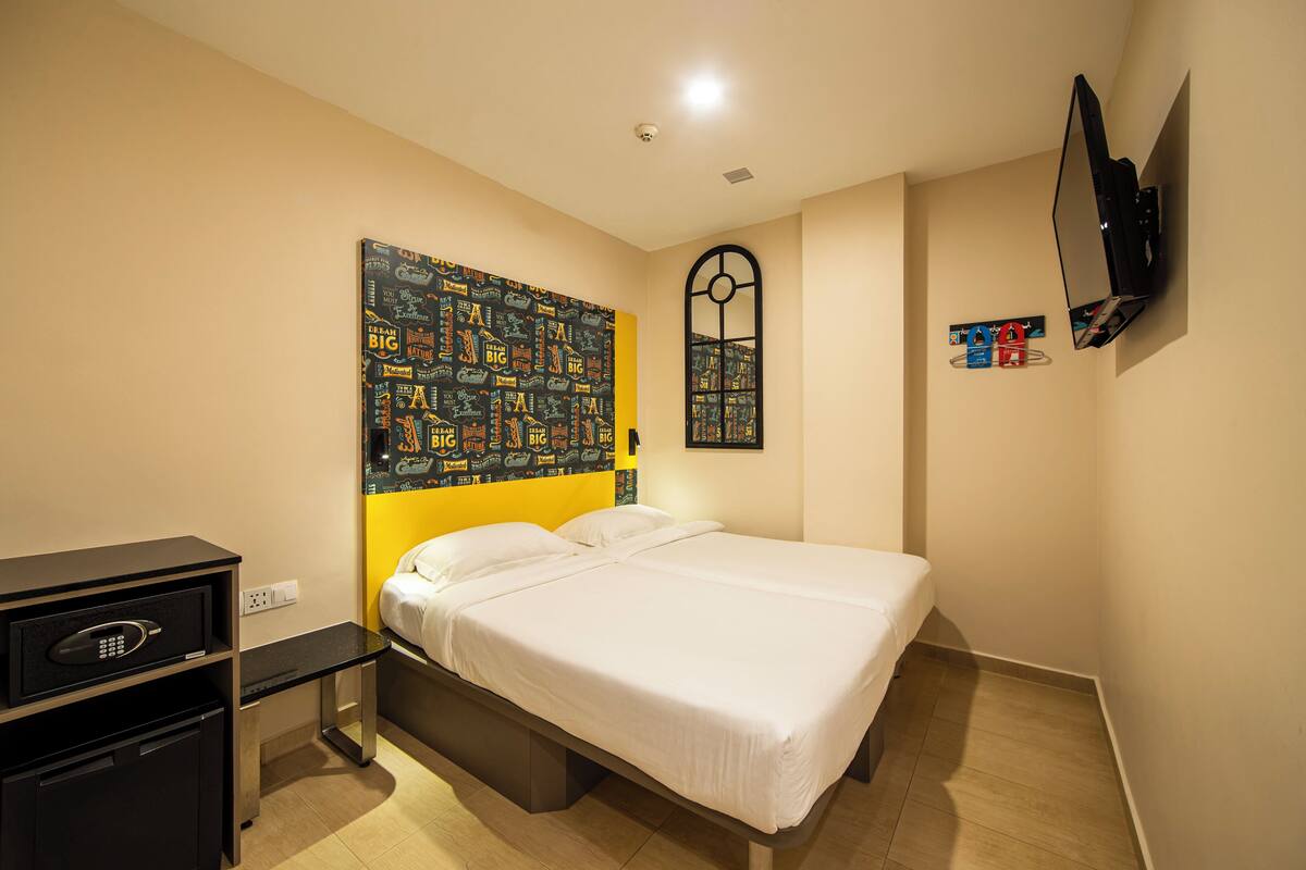 Une chambre d’hôtel comprenant un lit, un bureau avec un ordinateur, un téléviseur fixé au mur et une œuvre d’art originale au-dessus du lit.