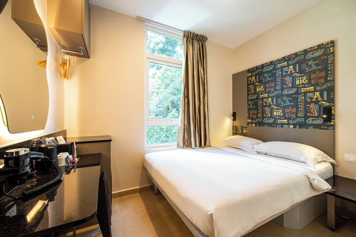 Une chambre d’hôtel comprenant un lit, un bureau avec un téléphone, une fenêtre avec des rideaux et un mur orné de citations inspirantes.