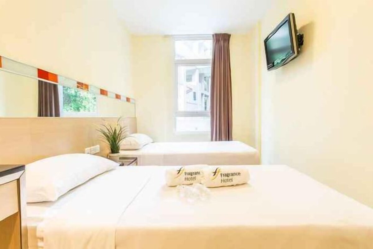 A hotel room with two beds, a television, a window with curtains, and a plant.