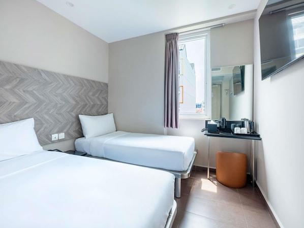 A hotel room with two beds, a desk with a mirror, a television, and a window with curtains. - ibis budget Singapore Dahlia (Singapore)