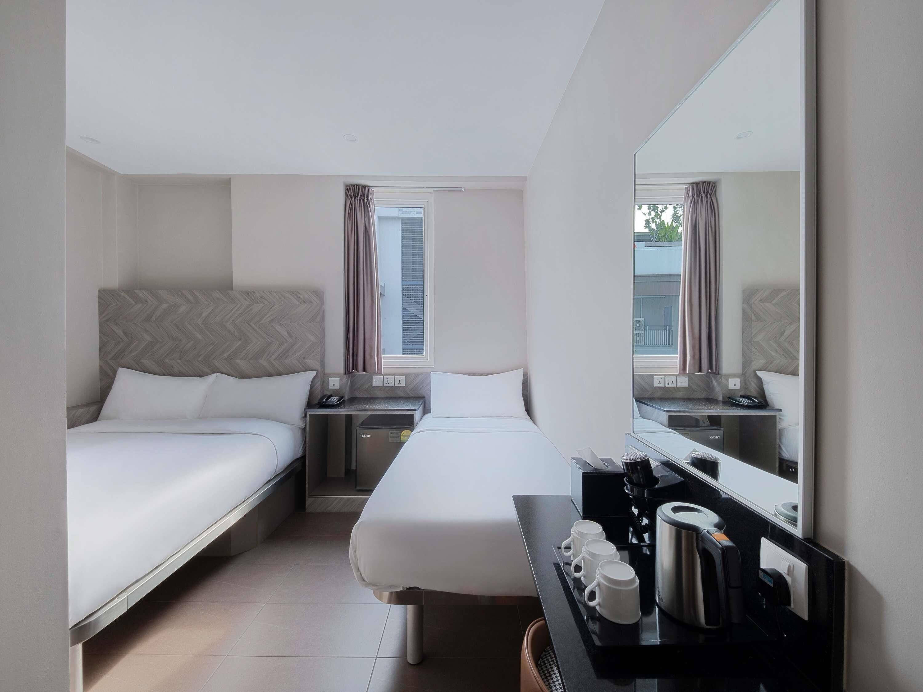 A hotel room with two beds, a desk with a coffee maker, and a large mirror.