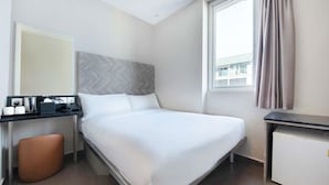 Una habitación de hotel con cama, escritorio, teléfono, cafetera y un taburete pequeño.