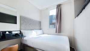 Una habitación de hotel con cama, escritorio, teléfono, silla y ventana con cortinas.