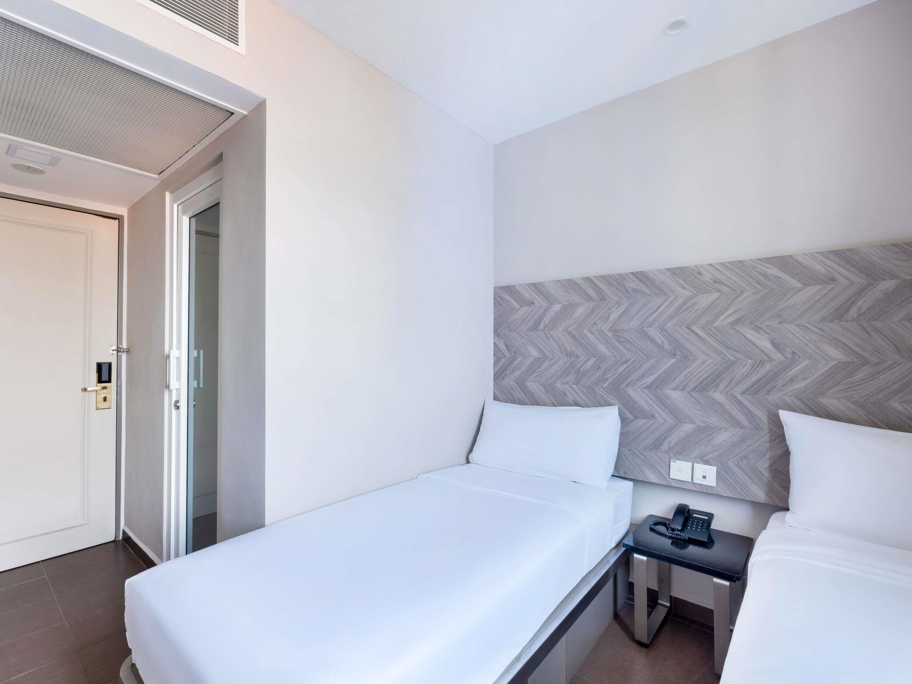A hotel room with a single bed, a bedside table with a phone, and a door with a handle.