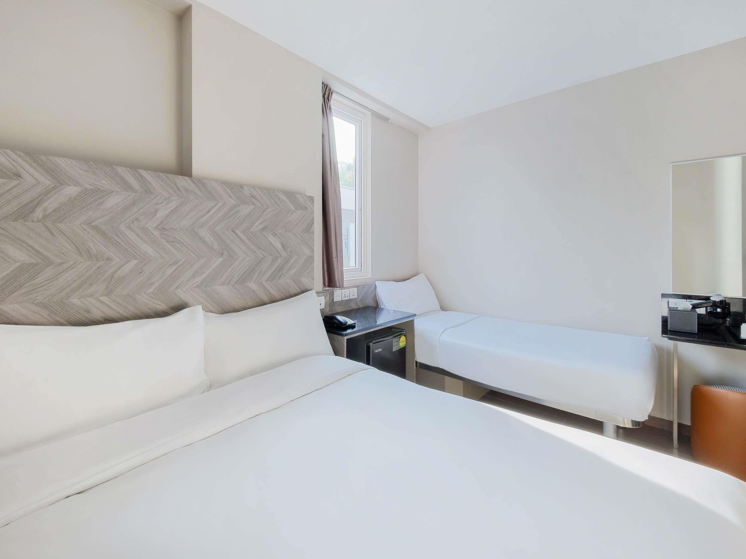 Une chambre d’hôtel avec deux lits, un bureau avec un téléphone et un miroir.