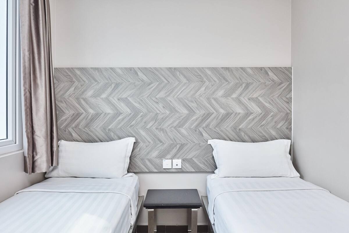 Habitación de hotel con dos camas, una mesita pequeña y un cabecero con estampado de espiga.
