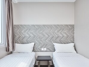 Habitación de hotel con dos camas, una mesita pequeña y un cabecero con estampado de espiga.