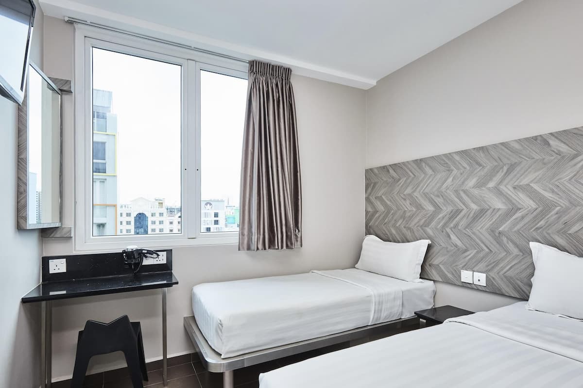 A hotel room with a bed, a desk, a chair, a window with curtains, and a city view.