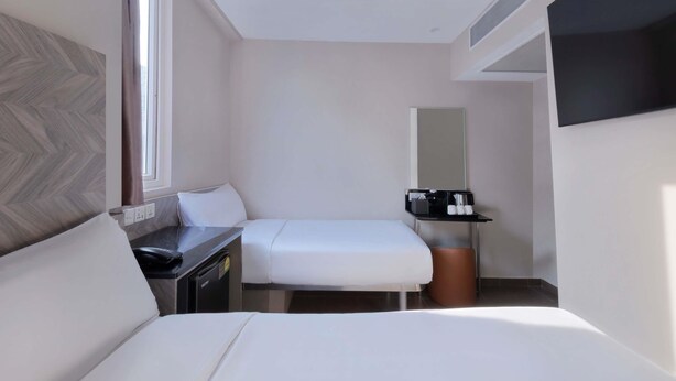 A hotel room with a bed, a desk, a chair, a TV, and a small table with a coffee maker and cups. - ibis budget Singapore Dahlia (Singapore)