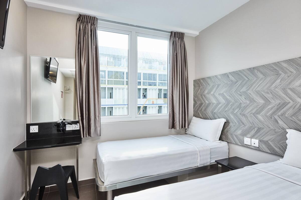 Habitación de hotel con cama, escritorio, silla y un ventanal con cortinas.