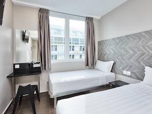 Habitación de hotel con cama, escritorio, silla y un ventanal con cortinas.
