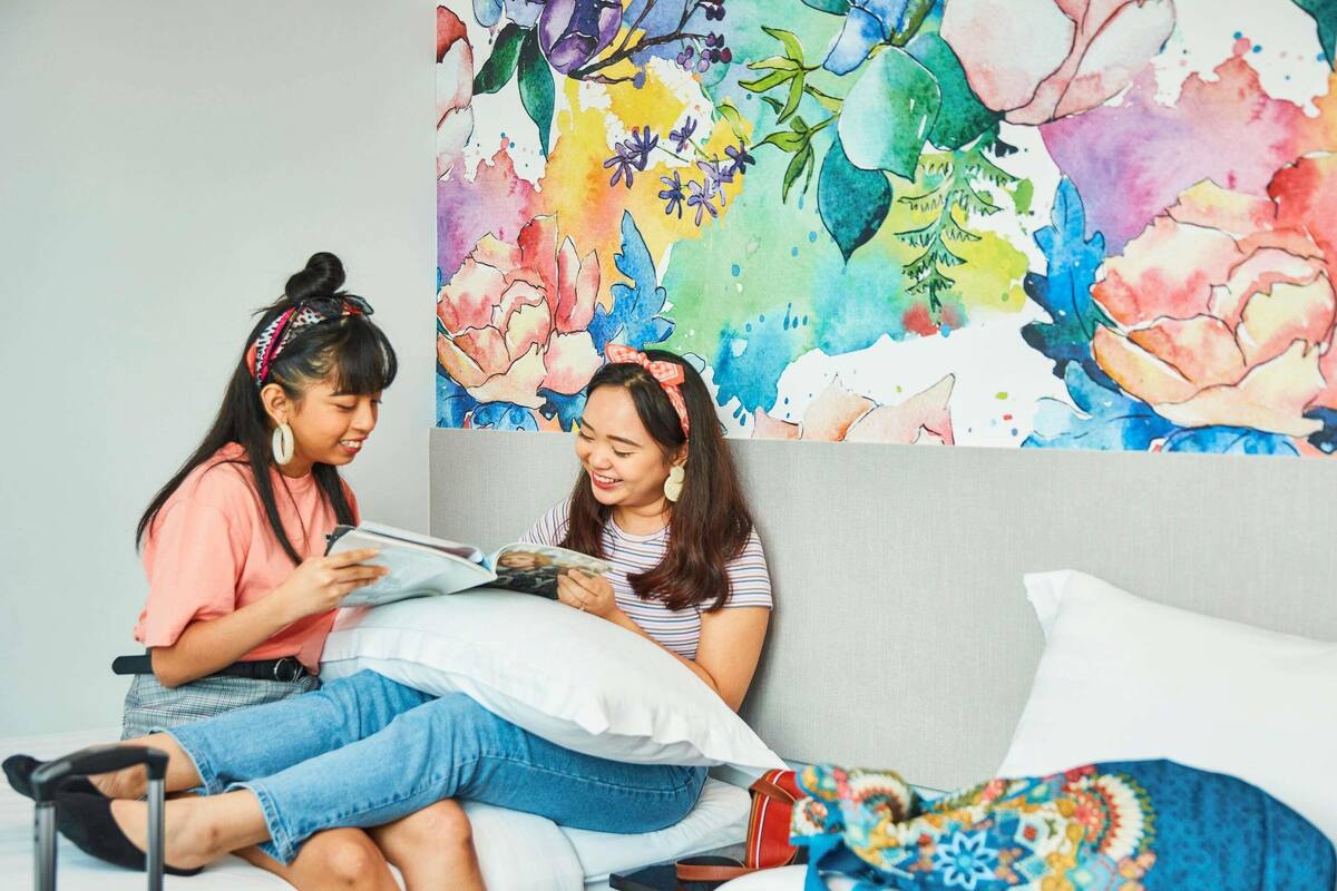 Two people sitting on a bed with a colorful floral wall art behind them.