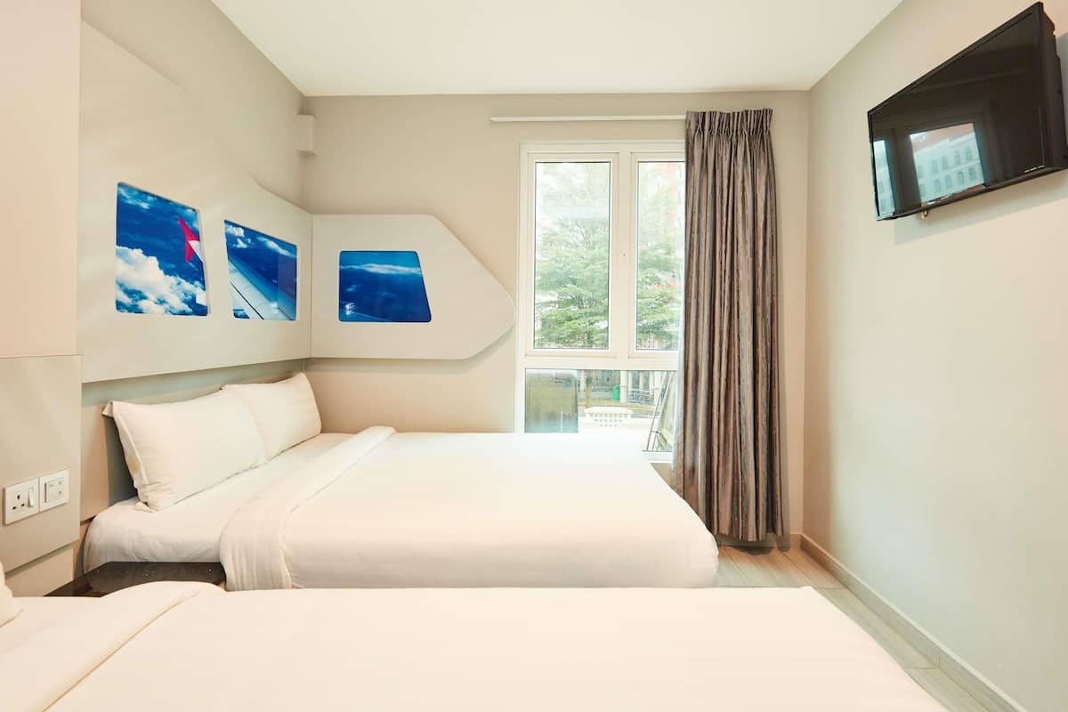 A bedroom with a large bed, a TV mounted on the wall, and a window with curtains.