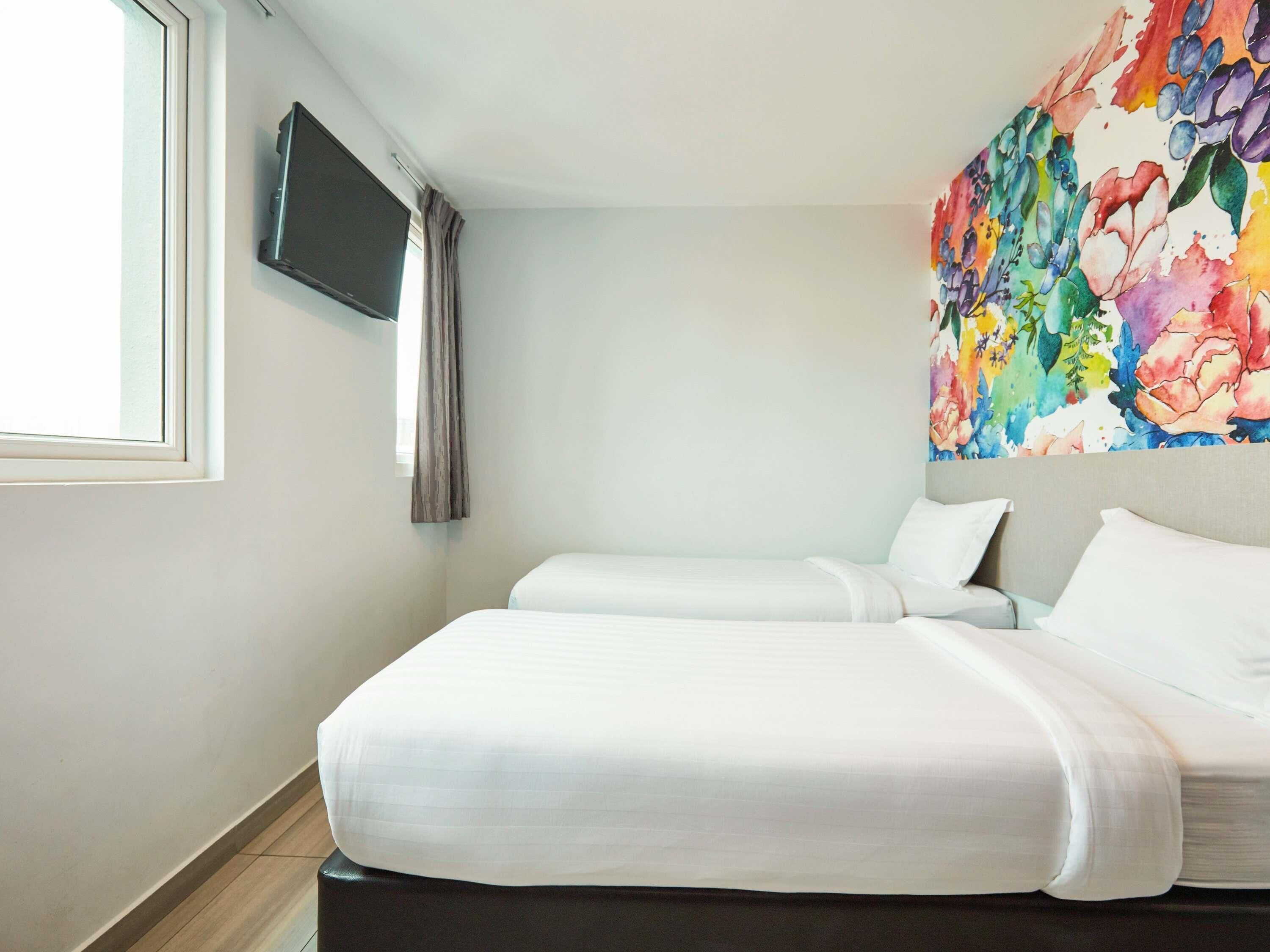 Une chambre d’hôtel avec deux lits, un téléviseur à écran plat fixé au mur et une œuvre d’art florale aux couleurs vives au-dessus des lits.