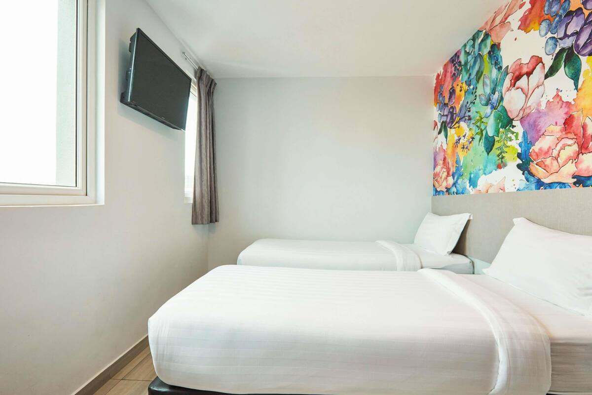 Une chambre d’hôtel avec deux lits, un téléviseur à écran plat fixé au mur et une œuvre d’art florale aux couleurs vives au-dessus des lits.