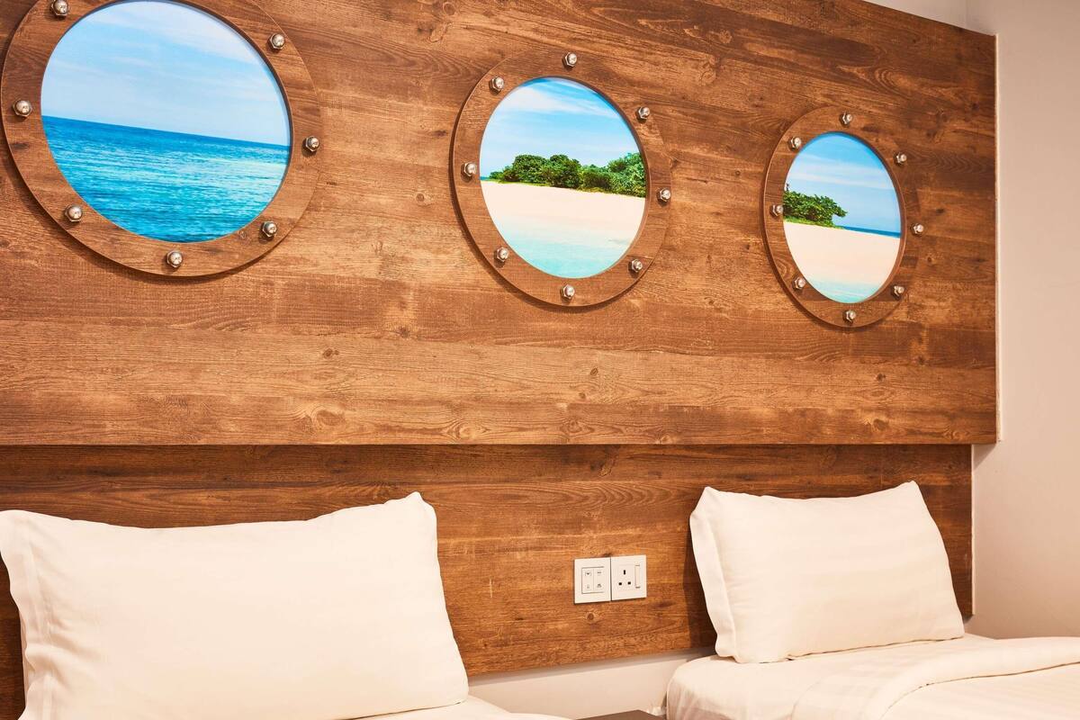 A hotel room with a wooden headboard featuring three circular mirrors with beach views. There are two beds with white bedding.