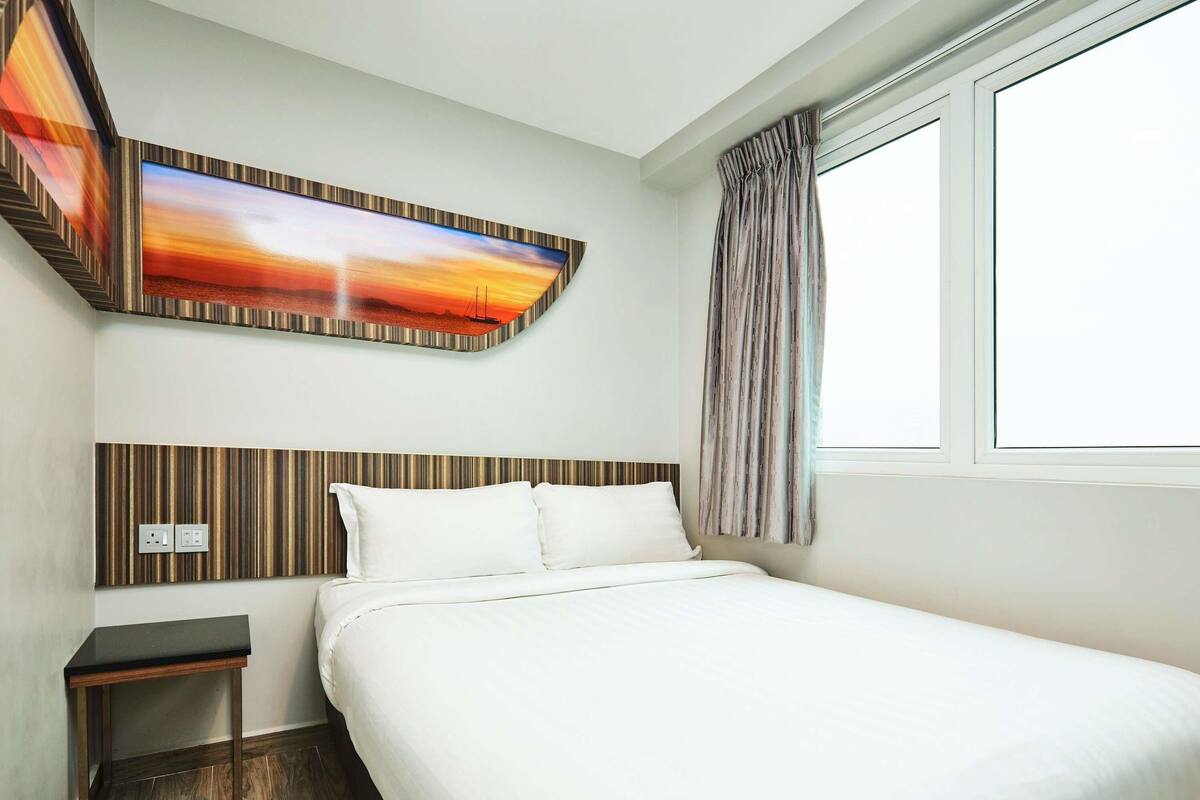 A hotel room with a bed, a nightstand, a painting, and a window with curtains.