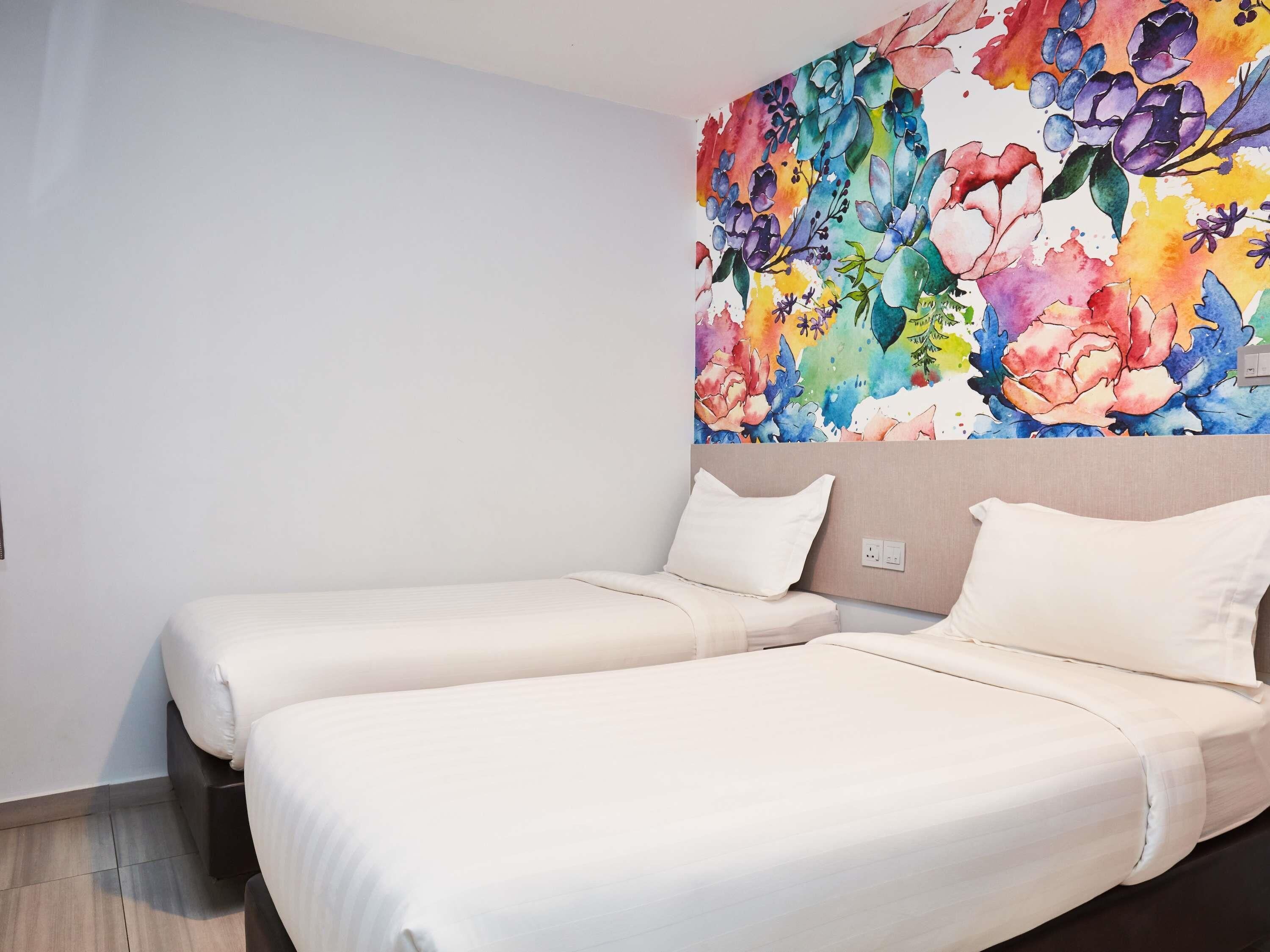 A hotel room with two beds, a colorful floral mural on the wall, and a neutral color scheme.
