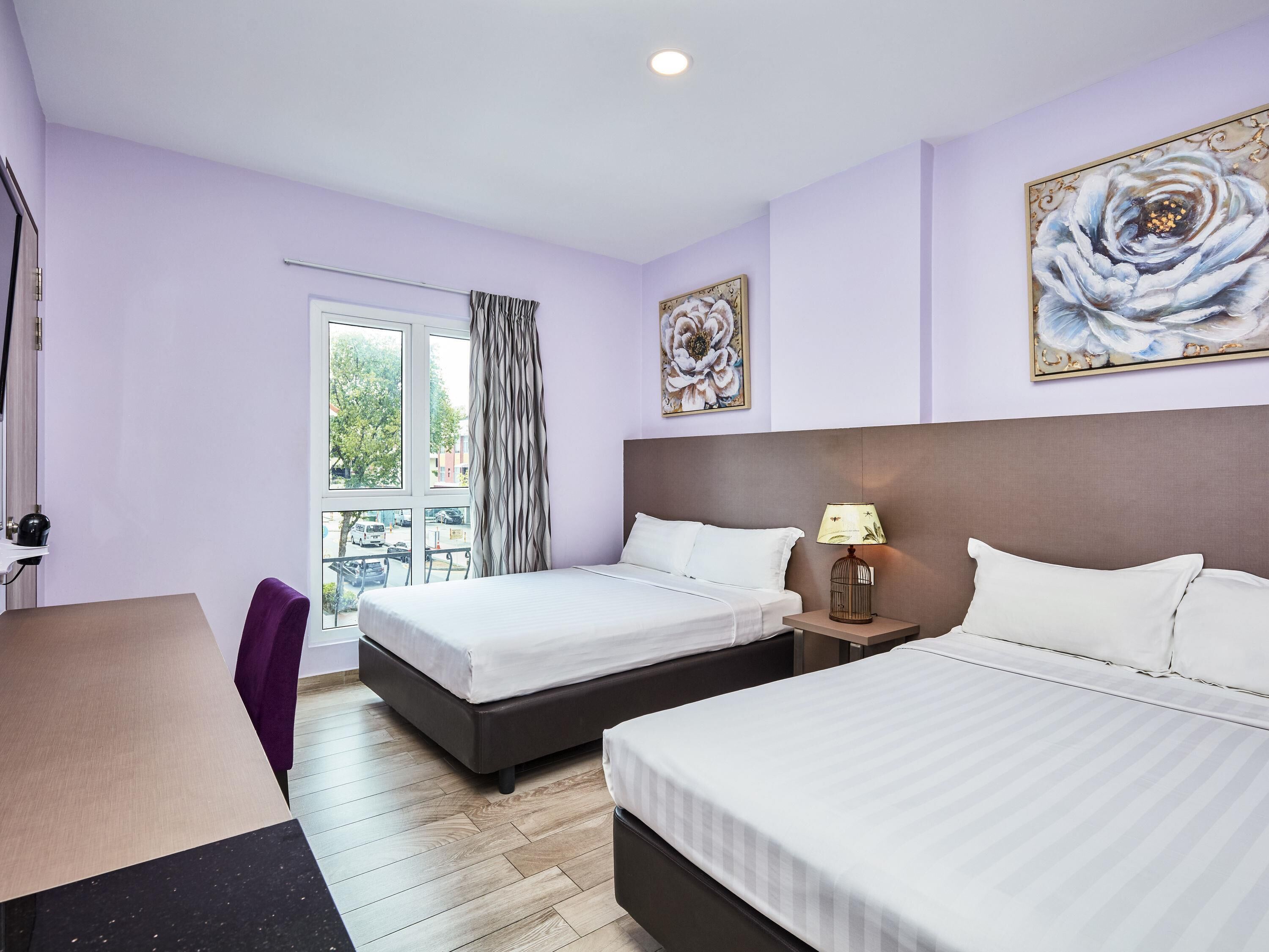 Ein Hotelzimmer mit zwei Betten, einem Schreibtisch, einem Stuhl und einem fensterbelagten Fenster.
