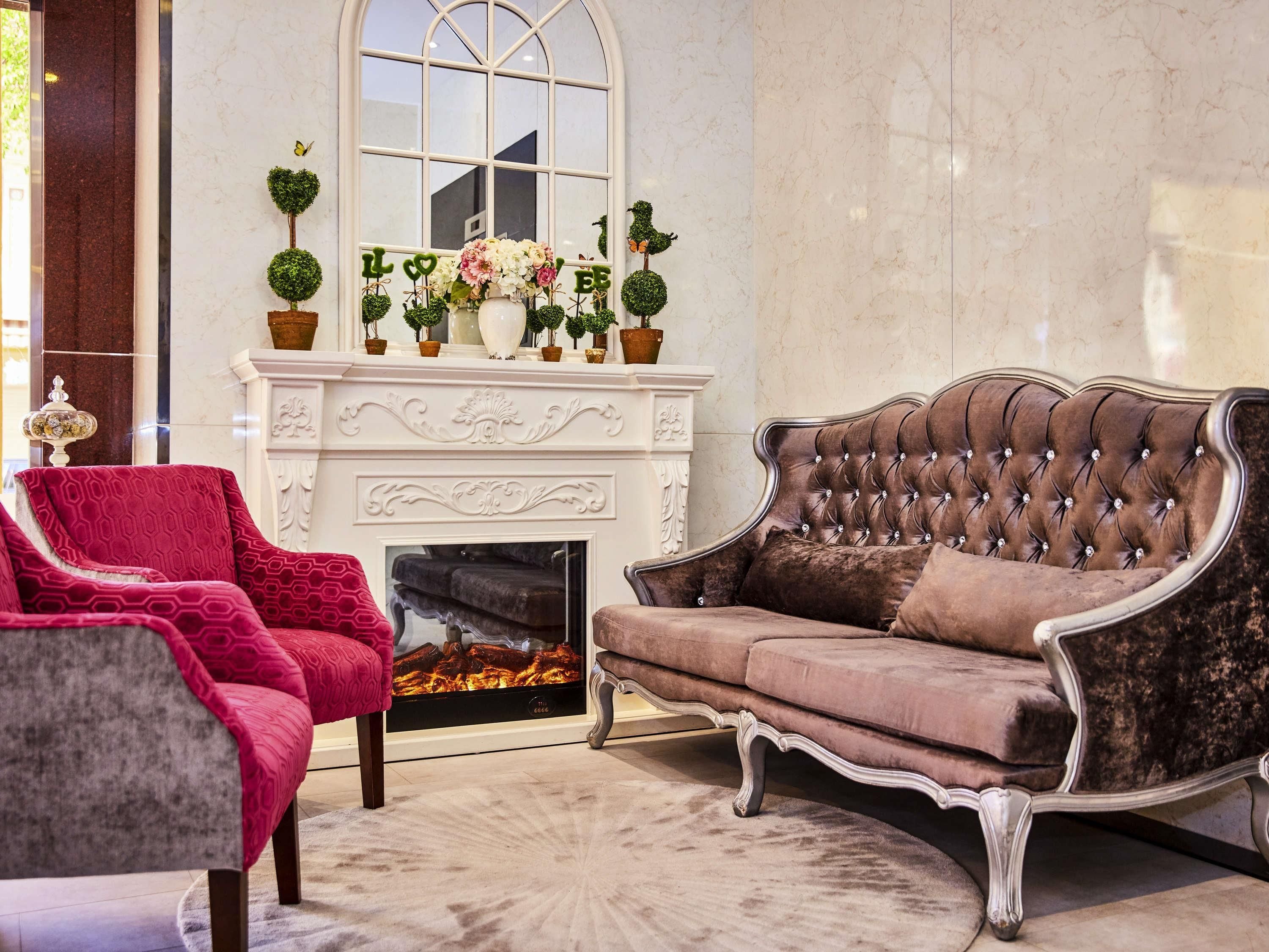Un salón lujoso con chimenea, un sillón rojo, un sofá marrón y plantas decorativas.