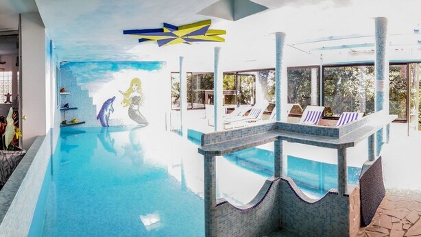 An indoor swimming pool with a mermaid mural, lounge chairs, and a checkered floor. - Hotel Soraya (Lignano Sabbiadoro)