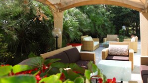 An outdoor patio with wicker furniture, a glass table, and a lamp post. - Hotel Soraya (Lignano Sabbiadoro)
