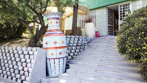 A staircase leading to a building with a green roof, surrounded by a wall of concrete blocks and a decorative vase. - Hotel Soraya (Lignano Sabbiadoro)