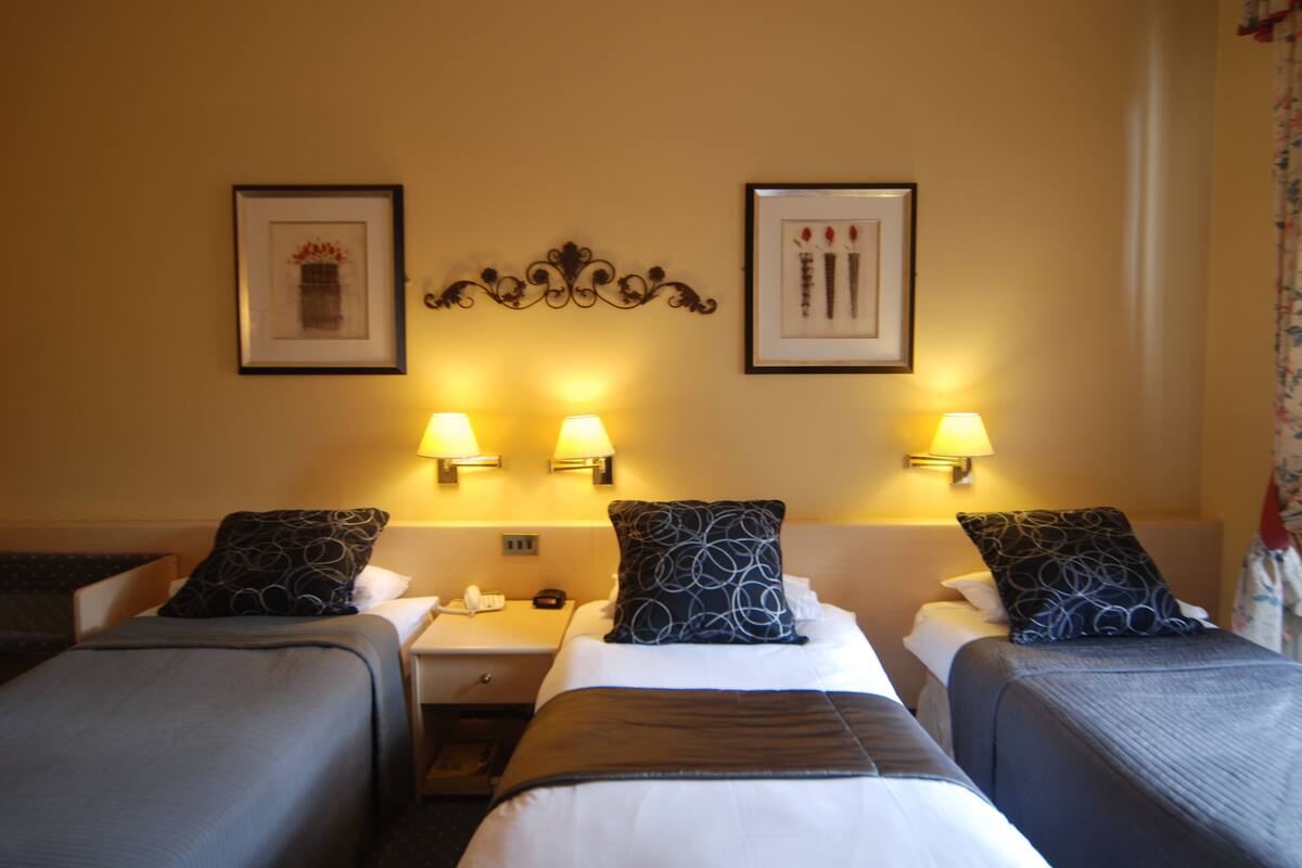 A hotel room with two single beds, a nightstand, a telephone, and two wall-mounted lamps.