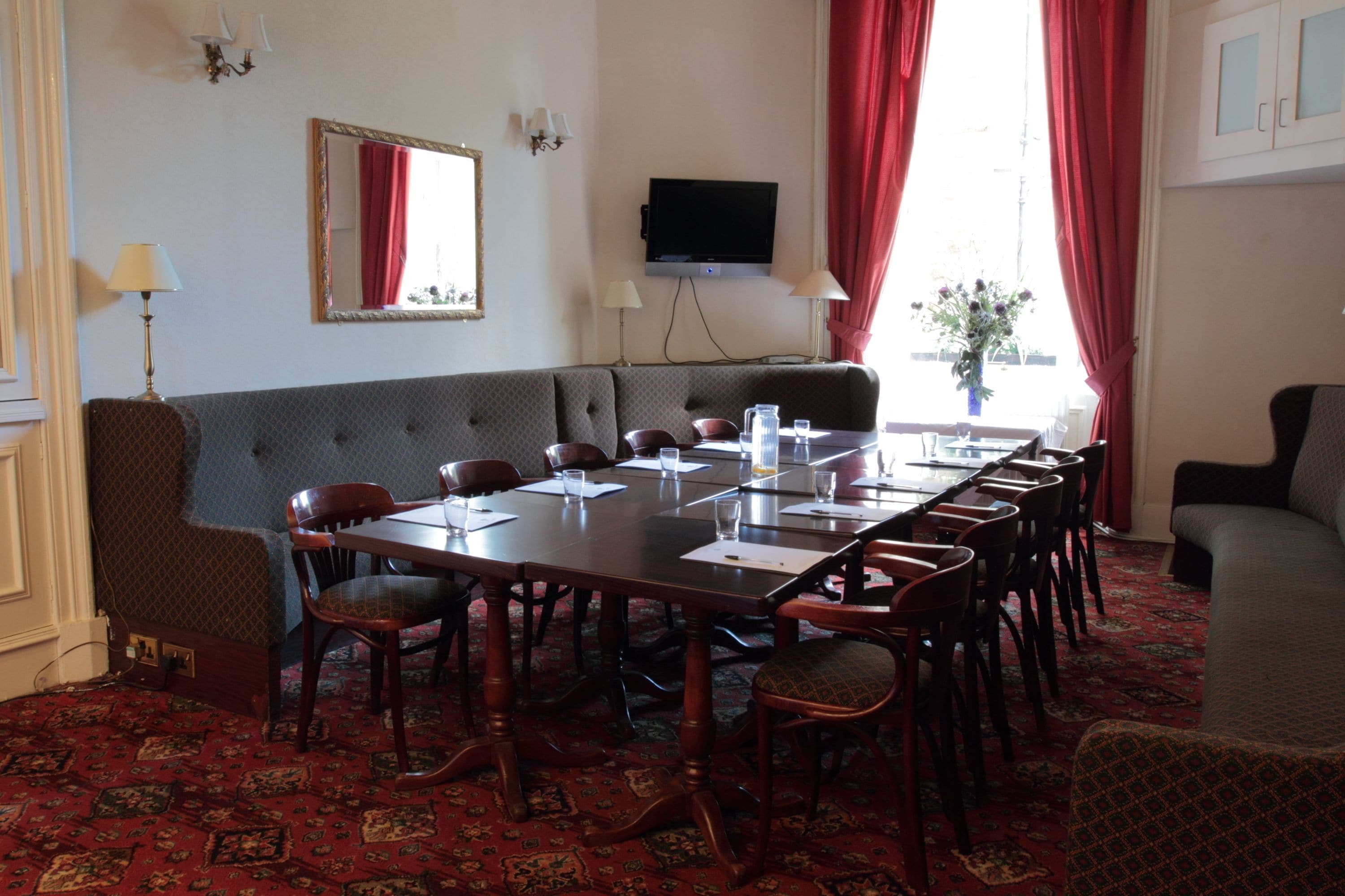 Une salle de conférence avec une longue table, des chaises, un canapé et un téléviseur fixé au mur.