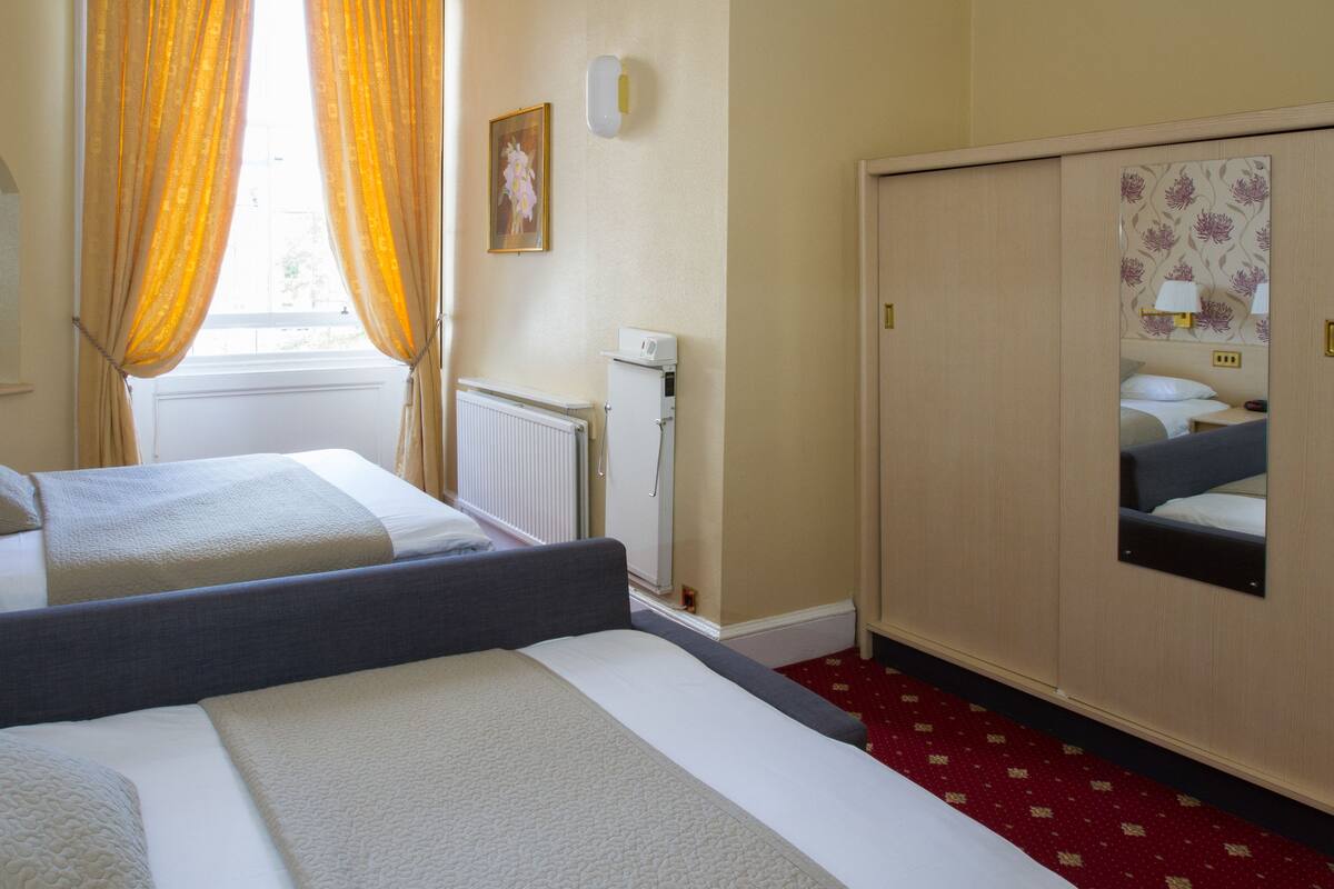 A hotel room with two beds, a radiator, a wardrobe, and a window with curtains.
