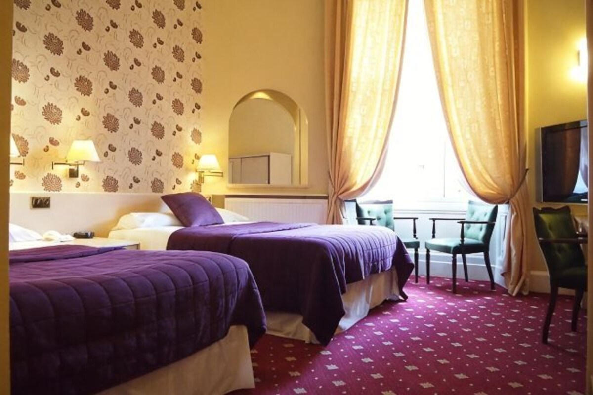 A hotel room with two beds, a desk, a chair, a TV, and a window with curtains.