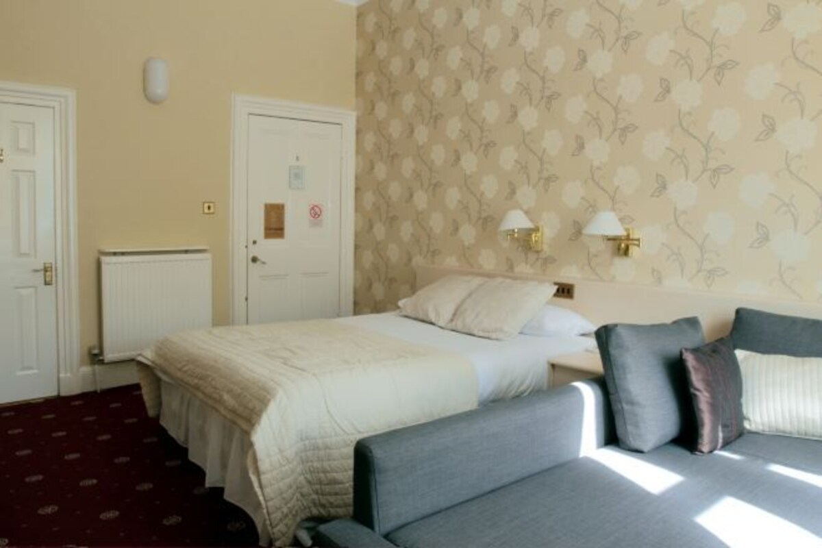 A bedroom with two beds, a radiator, a door with a sign, and a patterned wallpaper.