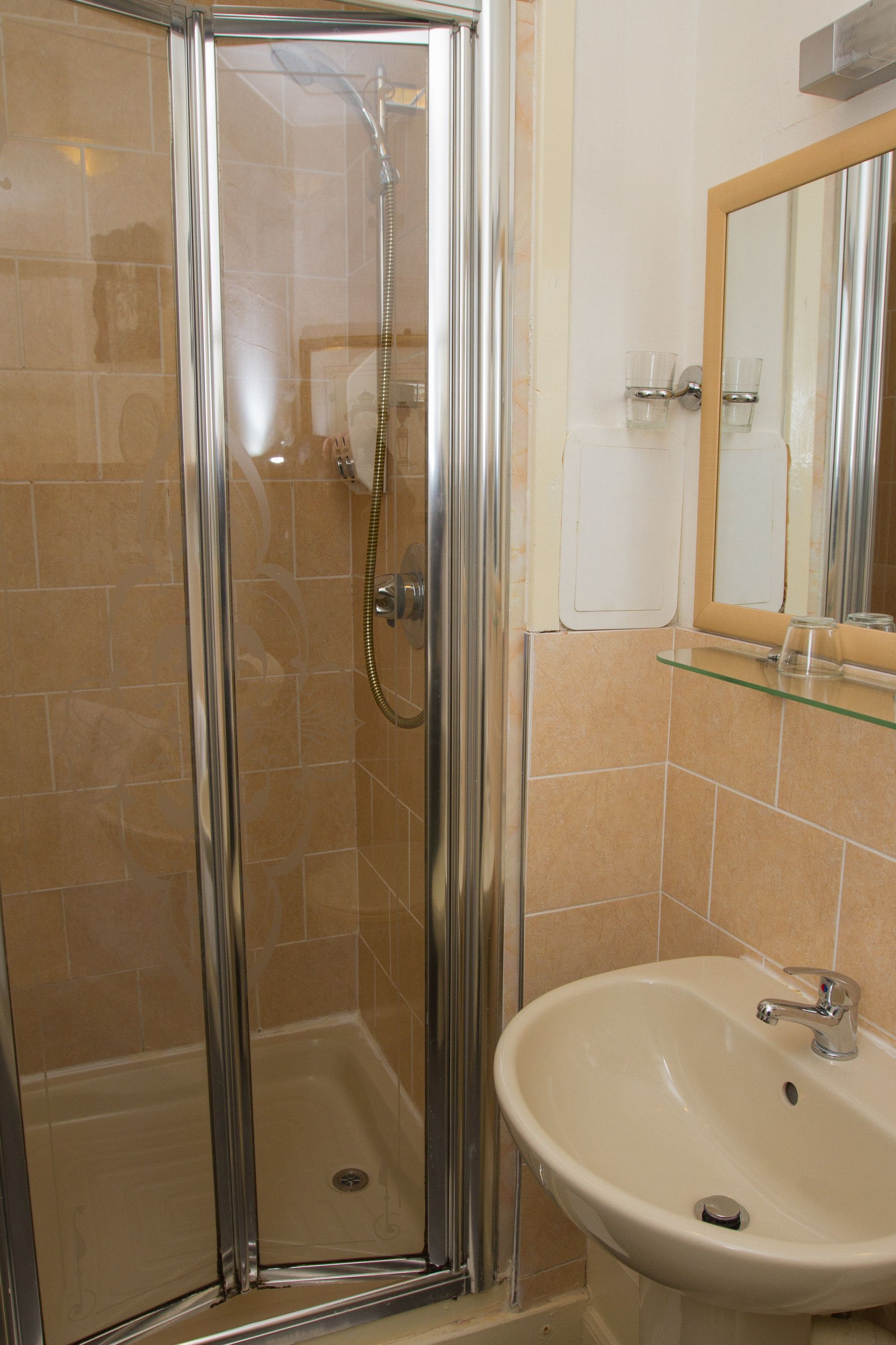 Een badkamer met een douche met glazen wand, een wastafel en een spiegel.