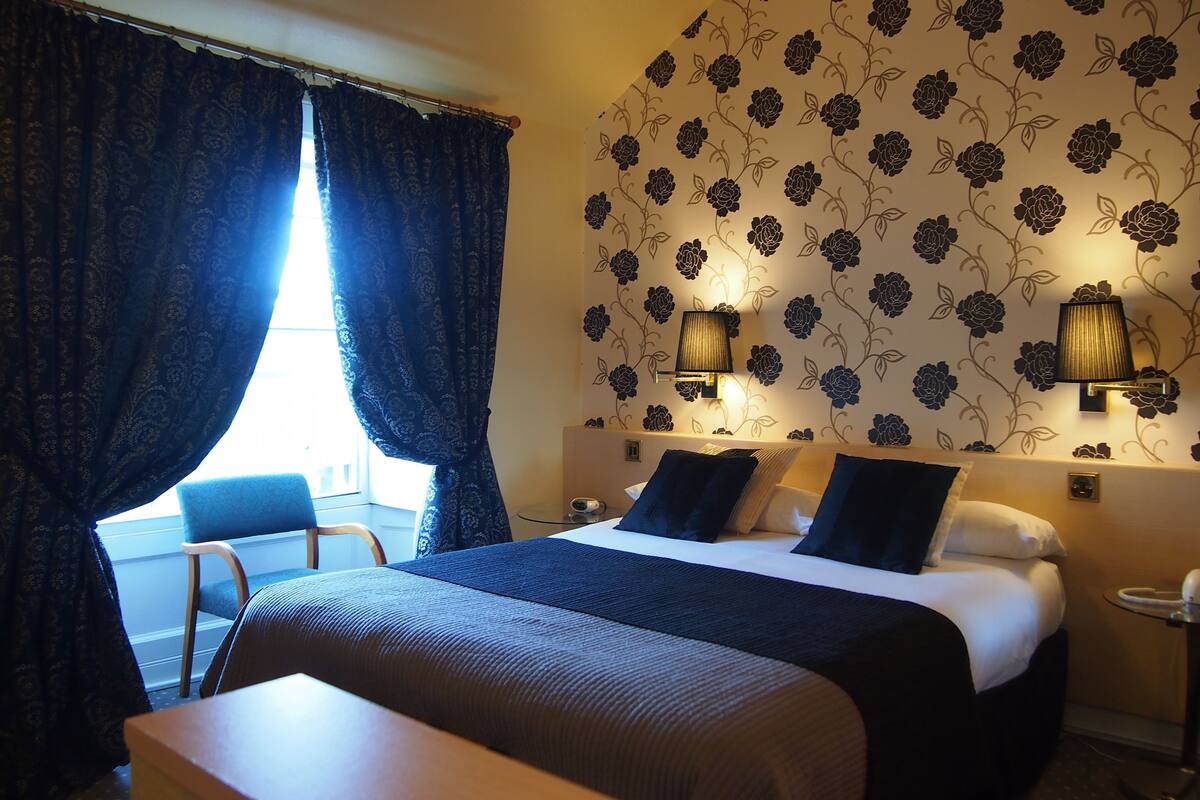A hotel room with a bed, two bedside lamps, a chair, and a small table.