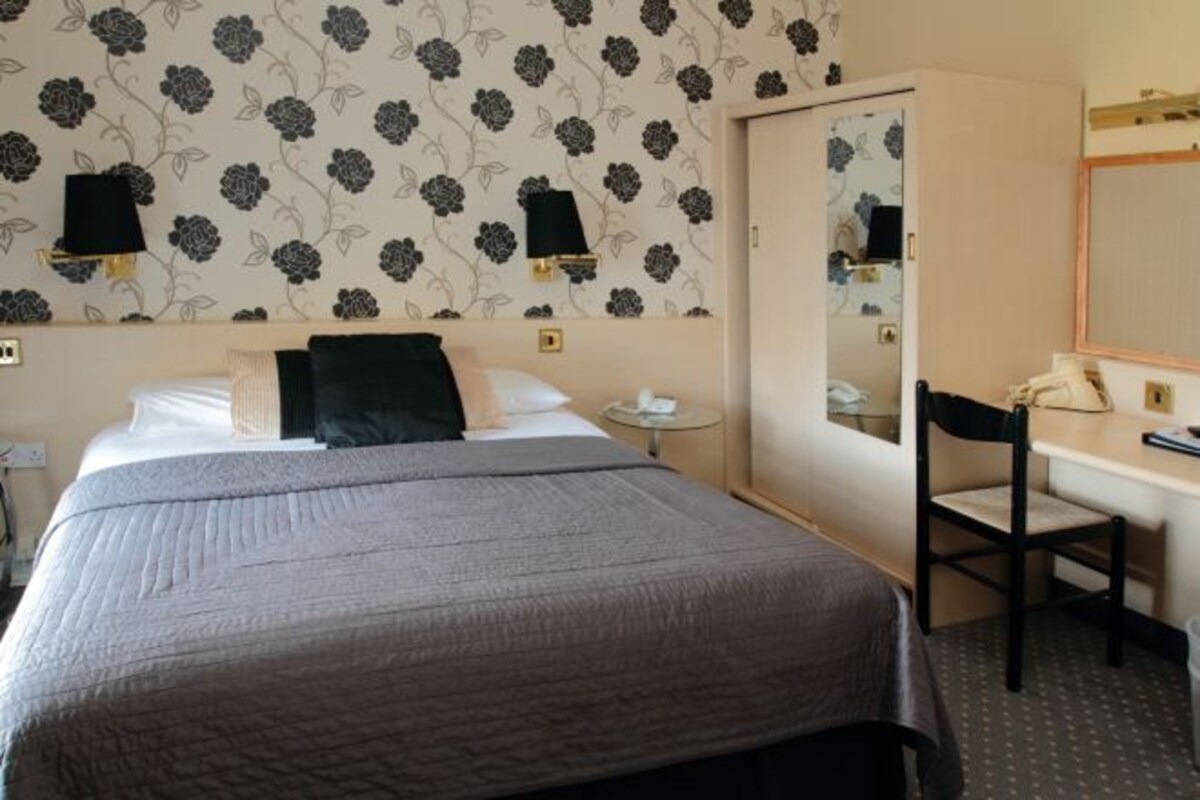 A hotel room with a bed, a desk, a chair, and a mirror.