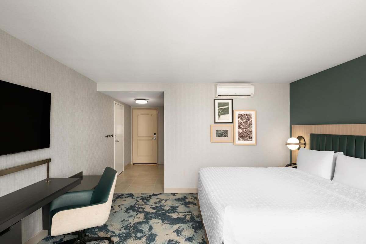 Hotelkamer met een bed, bureau, stoel, televisie, ingelijste foto’s en een airconditioning.