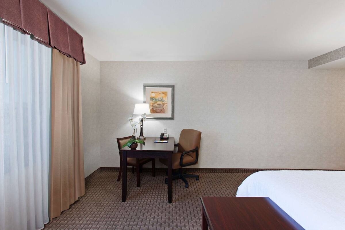 Une chambre d’hôtel avec un lit, un bureau doté d’une lampe, une chaise et un tableau accroché au mur.