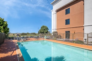 A swimming pool with a patio area, surrounded by a fence and a building with two windows.