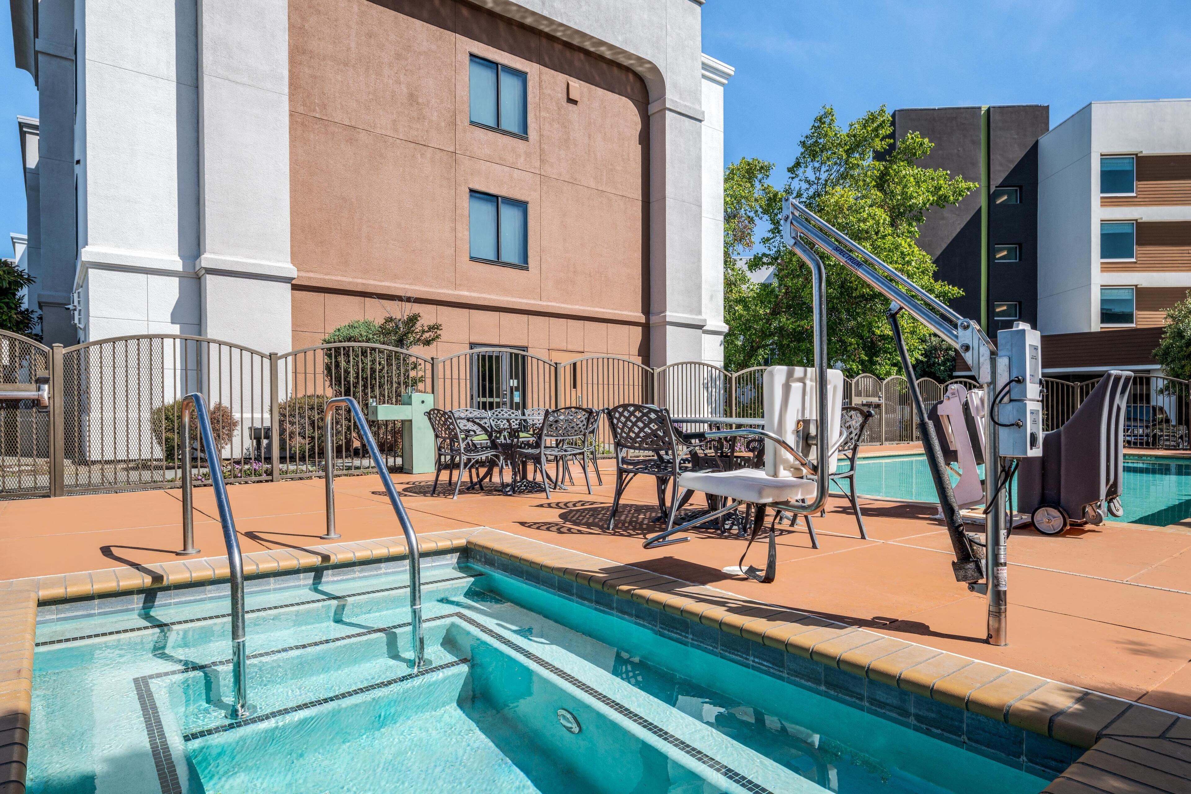Área de piscina com trampolim, espreguiçadeiras e um edifício ao fundo.