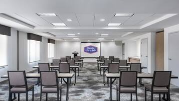 A conference room with a large screen displaying the Hampton Inn logo, rows of chairs, and a carpeted floor.