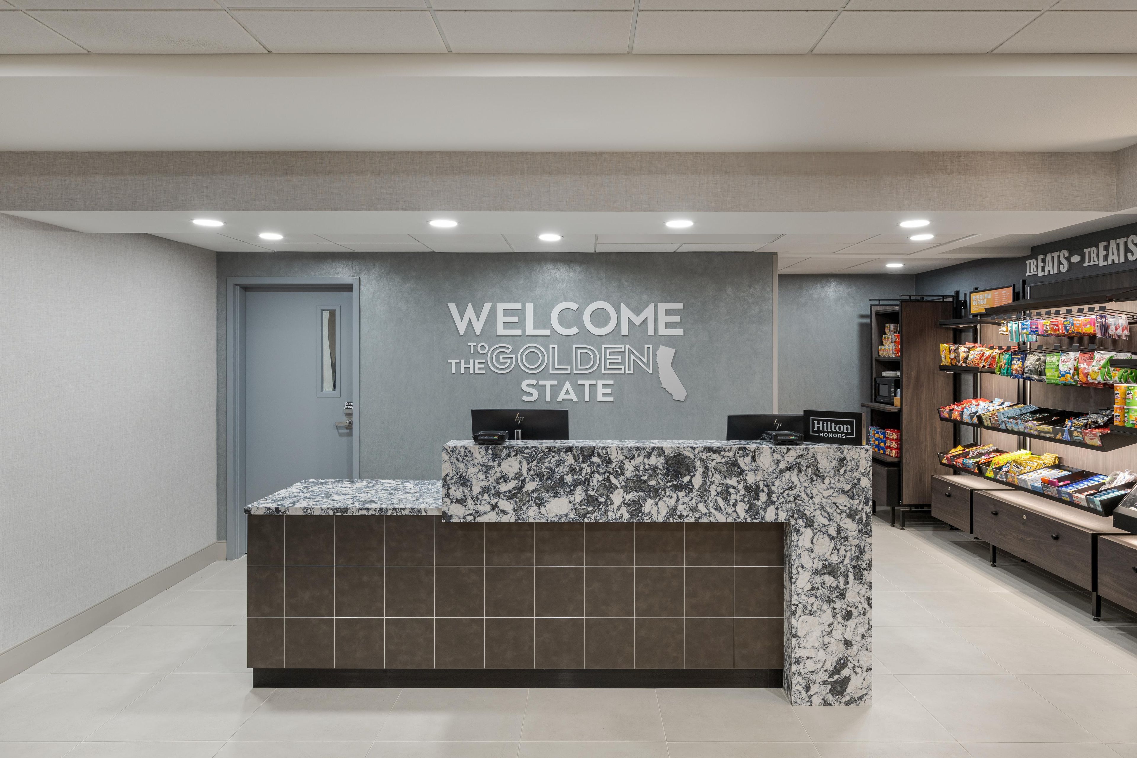 Una recepción con un letrero que dice 'Welcome to the Golden State', un minibar y un bar de aperitivos con diversos productos alimenticios.