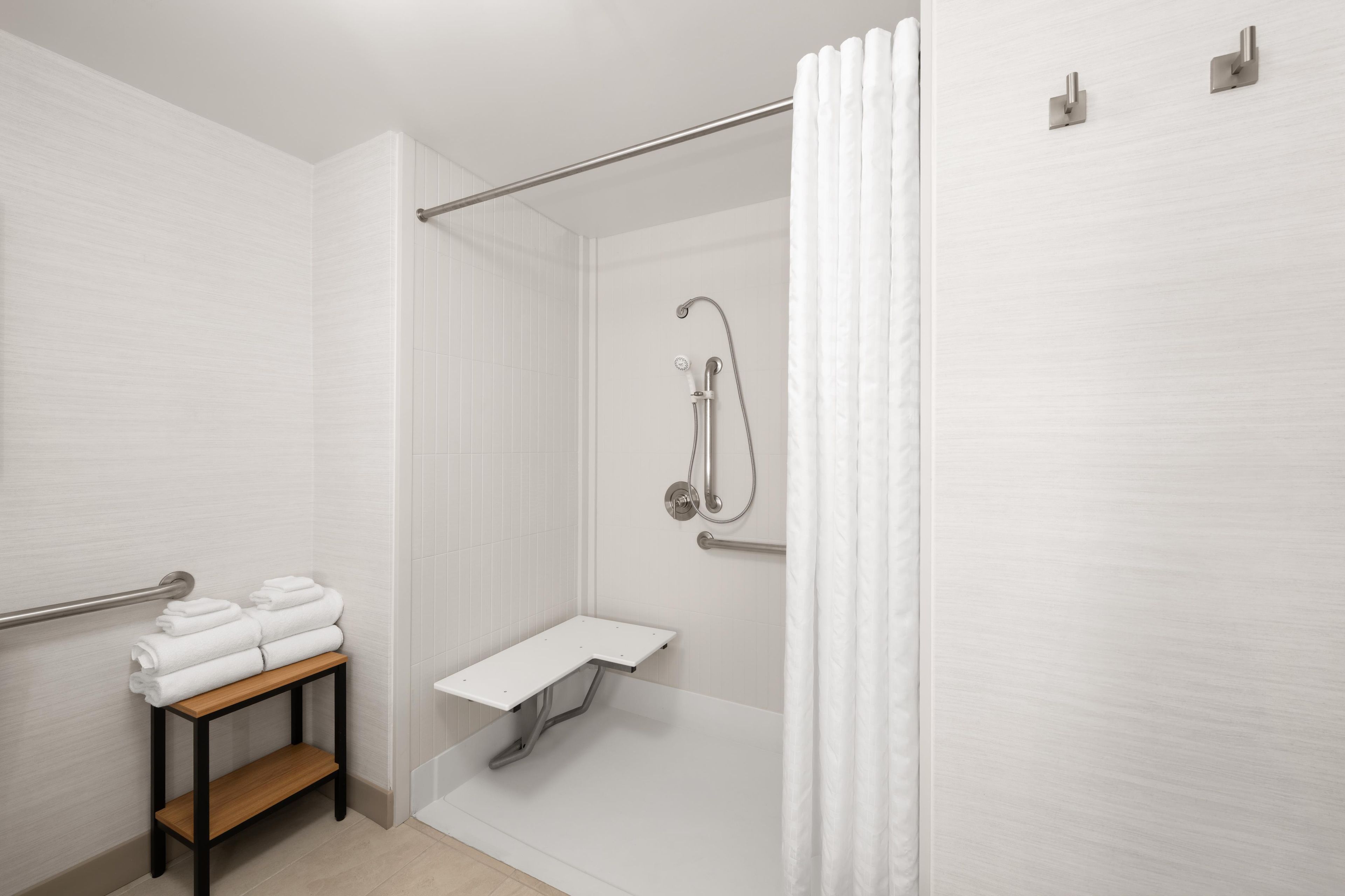 A modern bathroom with a shower, a towel rack, and a small shelf.